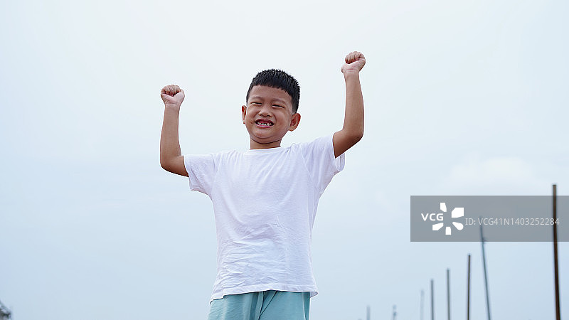 微笑的亚洲小男孩展示他的肱二头肌，象征着力量和成长图片素材