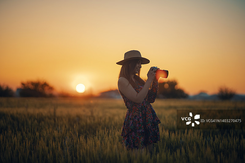 女摄影师拍摄日落时分的金色田野图片素材