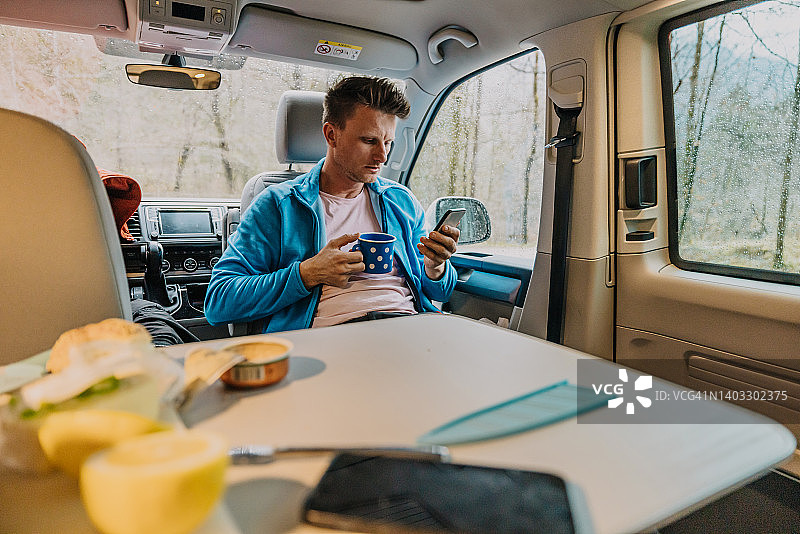 在露营车里喝咖啡时使用智能手机的男人图片素材