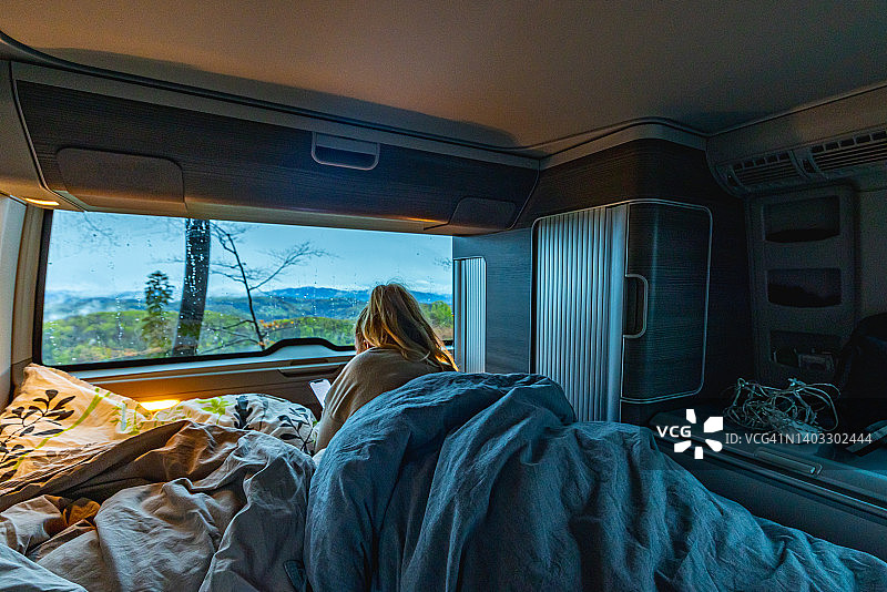 在露营拖车里放松，裹着毯子用手机的无忧无虑的女人图片素材