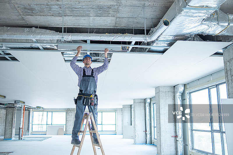 在建筑工地的梯子上拿着大型水平仪的快乐年轻建筑工人图片素材