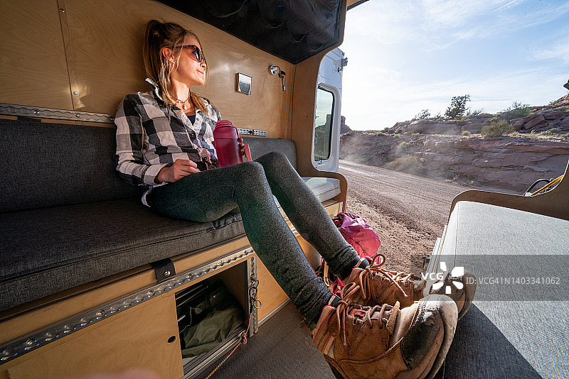 年轻女子在犹他州摩押附近的房车里放松身心，喝着水瓶里的水，欣赏美丽的风景图片素材