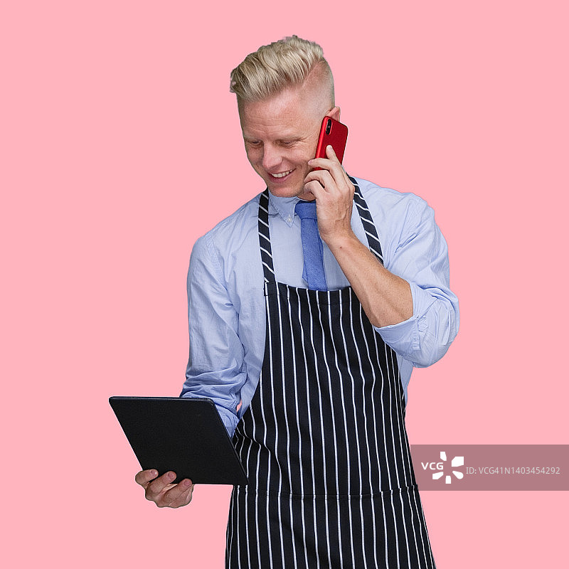 站在彩色背景前，穿着围裙，使用平板电脑的白人男屠夫图片素材