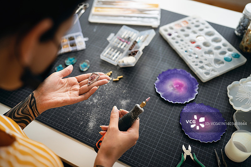 白人工匠女人用手动研磨机研磨她在工作室制作的环氧树脂珠宝图片素材