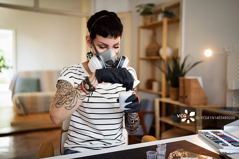 白人手工艺人在杯中用木棍混合环氧树脂，佩戴呼吸面罩图片素材