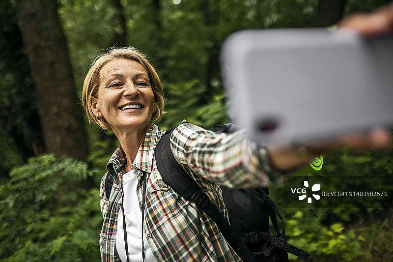 微笑的女人在森林里用智能手机自拍图片素材