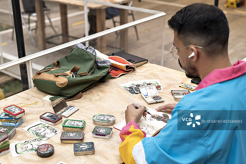 在桌子上的小笔记本上用水彩绘画的年轻男人图片素材