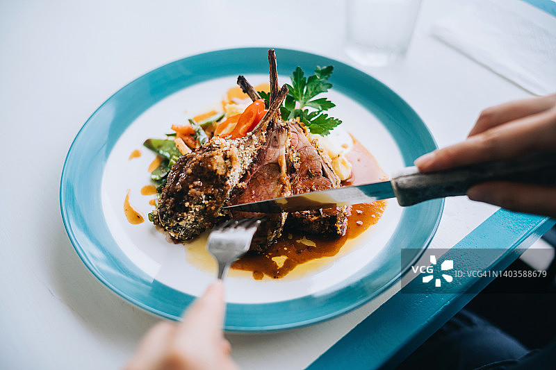 女人在高级餐厅享用午餐，吃羊排、土豆泥和烤蔬菜的局部照片图片素材