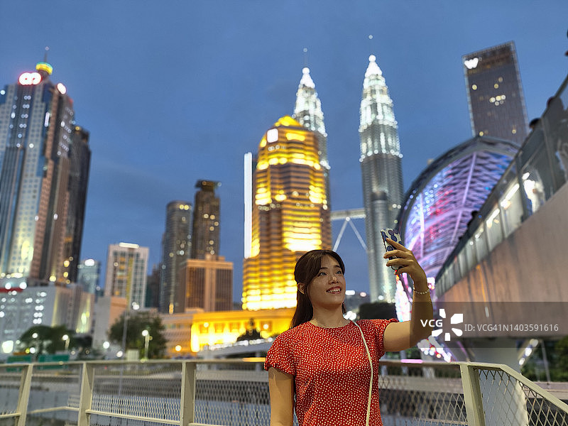 年轻亚洲女性在城市景观上用智能手机进行视频通话图片素材