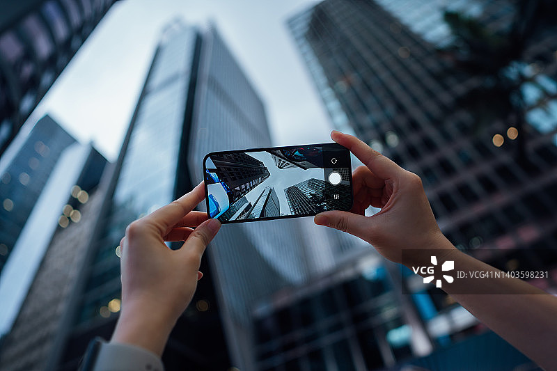 女人用智能手机拍摄市中心城市摩天大楼的个人视角图片素材