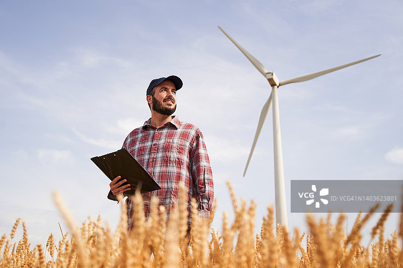 工程师站在麦田和风力涡轮机旁的低角度特写照片图片素材