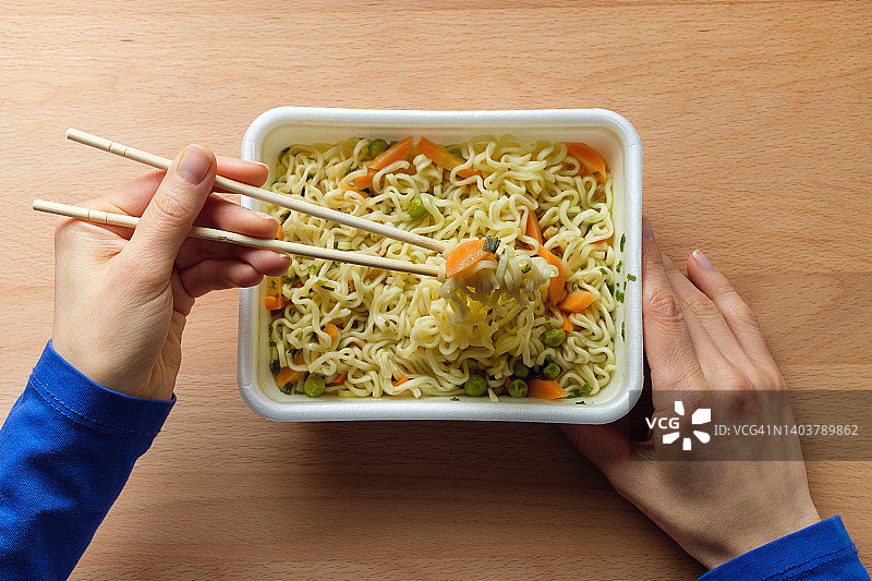 女人吃加了香料、蔬菜、香草和冻干肉的方便面。女孩用木筷子端着亚洲鸡肉拉面图片素材