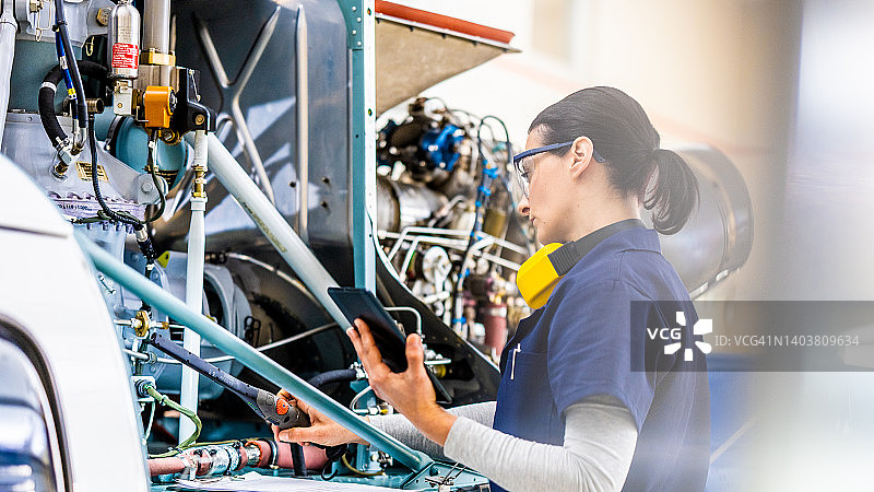 身穿制服的女航空工程师正在检查私人直升机，侧视图图片素材
