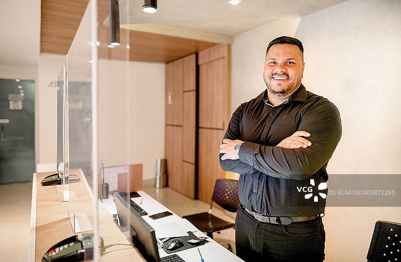 酒店经理站在登记入住柜台后，对着镜头微笑图片素材