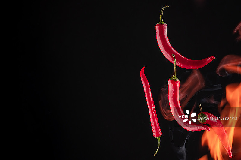 黑色背景上带有火焰的飞行的红辣椒图片素材
