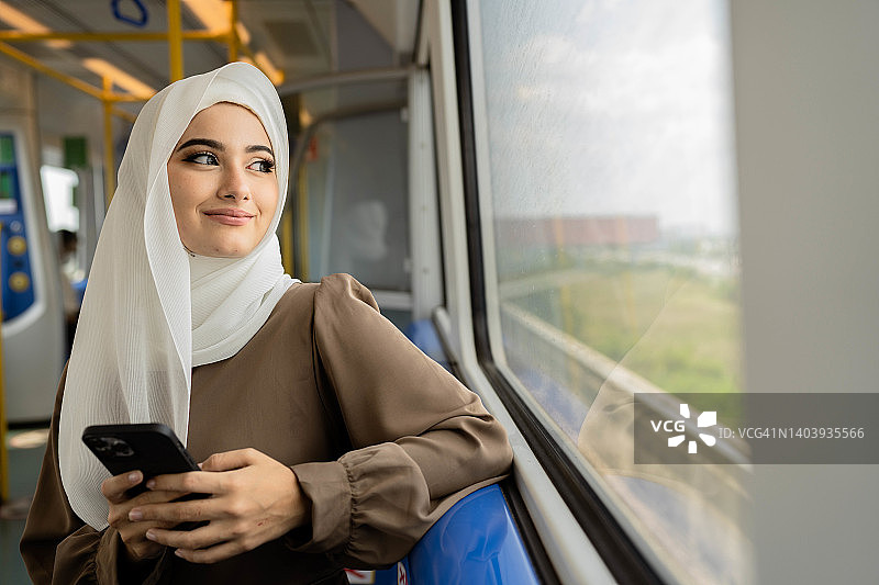 快乐的穆斯林女性在公共交通工具上用手机交谈。图片素材
