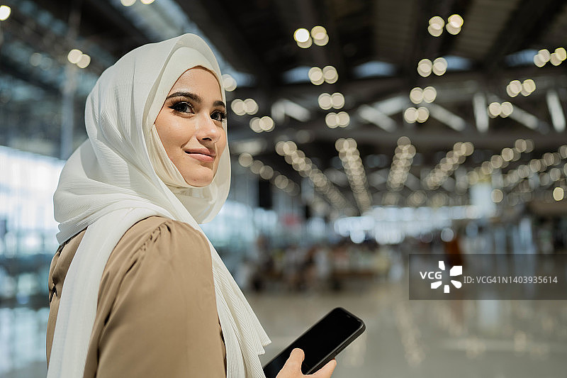 戴穆斯林头巾的亚洲商人在机场使用智能手机图片素材