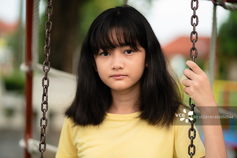一位患有精神疾病的女孩坐在秋千上看着镜头的正面肖像图片素材