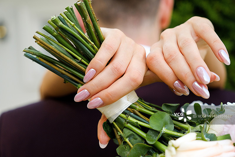 新娘和新郎的特写镜头，新娘拿着一束美丽的粉白色鲜花和绿叶。婚礼当天，庄严的仪式。图片素材