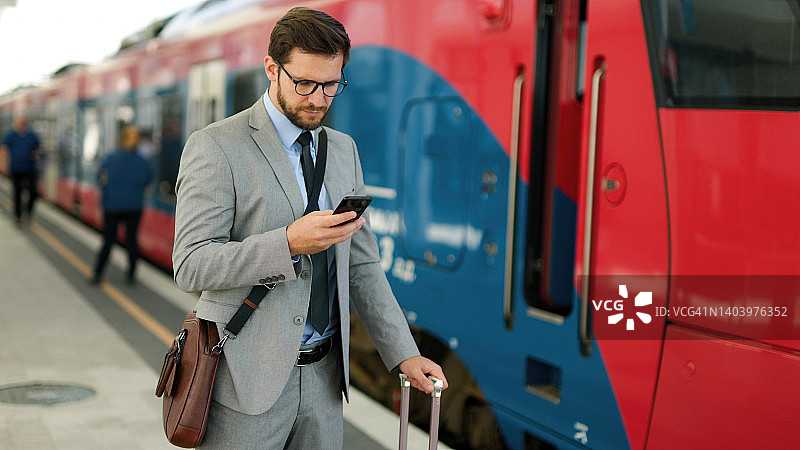 携带行李在火车站使用智能手机的中年商人图片素材