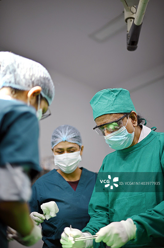 资深外科医生在手术室进行手术，助理医生/护士协助图片素材