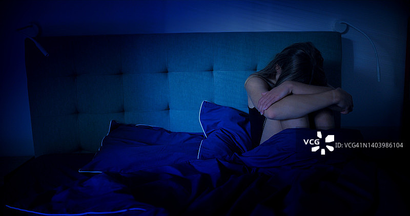 女人在床上恐惧地抱住膝盖图片素材