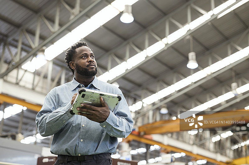 制造业中客户对产品质量的期望。一位非裔美国男性生产经理手持平板电脑，在塑料汽车零件的生产线上计划控制生产，以满足质量要求。图片素材