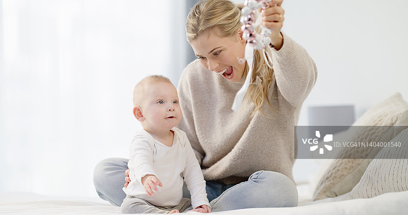 白人母亲和宝宝在明亮的白色卧室里一起玩耍，年轻母亲看着可爱的儿子对着玩具微笑。现代单亲育儿和儿童保育图片素材