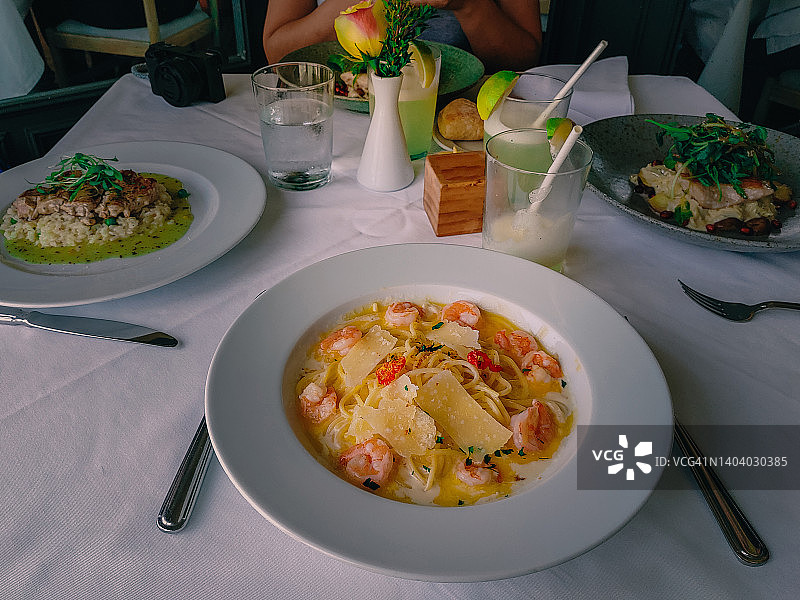 虾仁意面放在餐桌上的盘子特写，桌上还有其他三道菜和饮料。图片素材