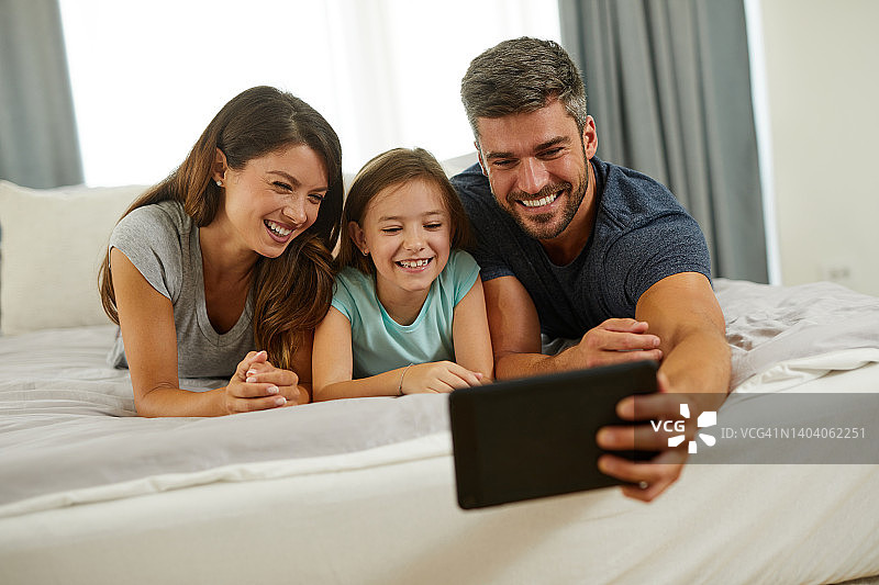 一家人在家里的床上用智能手机自拍图片素材