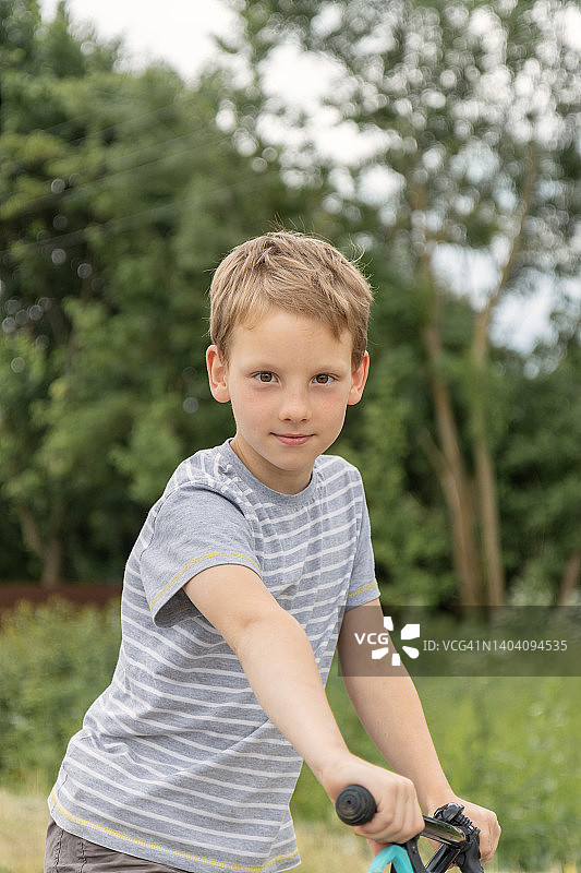 穿着T恤在户外骑自行车的微笑男孩图片素材