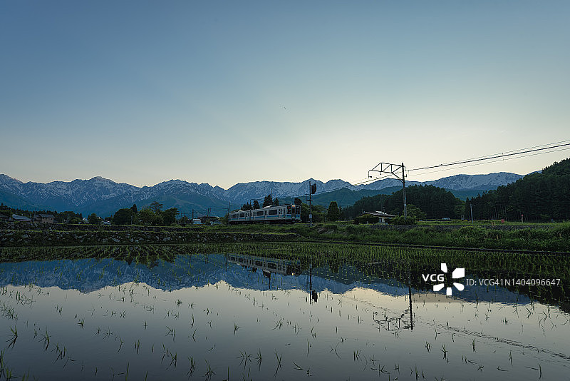 白马岳和北部阿尔卑斯山倒映在稻田中，一列当地火车经过图片素材