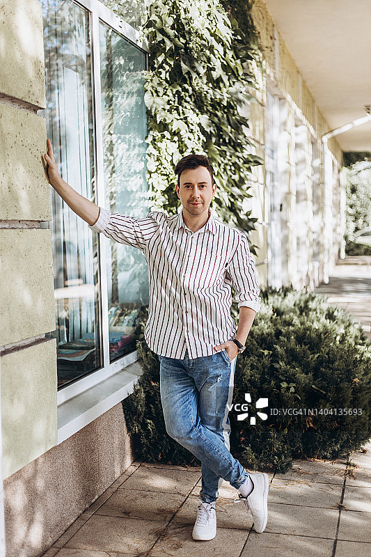 年轻男人靠在有植物墙的建筑旁图片素材