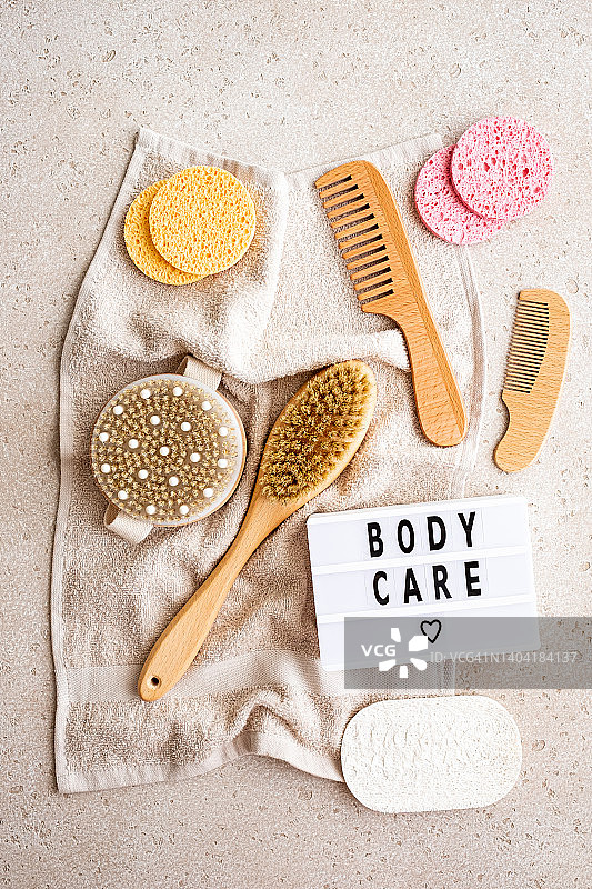 家用SPA设备（棉毛巾、木制身体刷、发刷、清洁海绵、丝瓜络海绵），用于身体和头发护理，以及带有“身体护理”字样的灯箱，混凝土背景，俯视图。可持续的生活方式。零浪费概念。图片素材