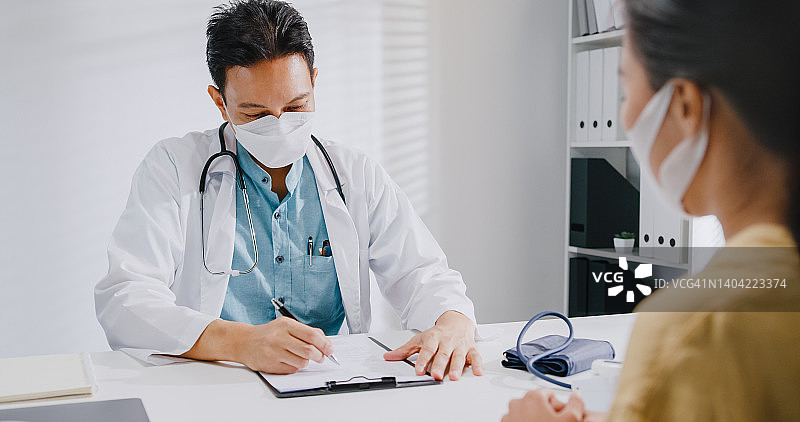 年长的亚洲男医生在诊所与女病人咨询时查看医疗结果，佩戴防护口罩图片素材