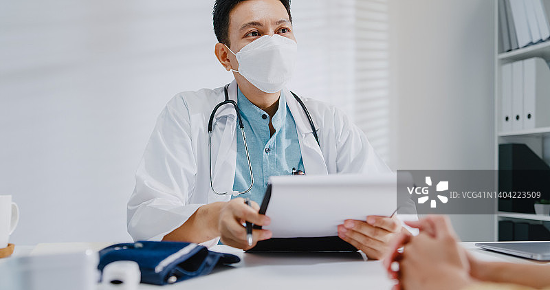 年长的亚洲男医生在诊所与女病人咨询时查看医疗结果，佩戴防护口罩图片素材