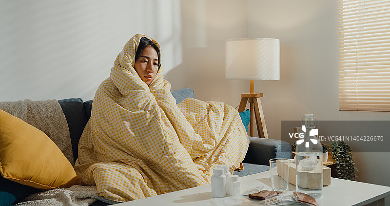 年轻的亚洲女人发烧咳嗽，在客厅沙发上盖着毯子图片素材