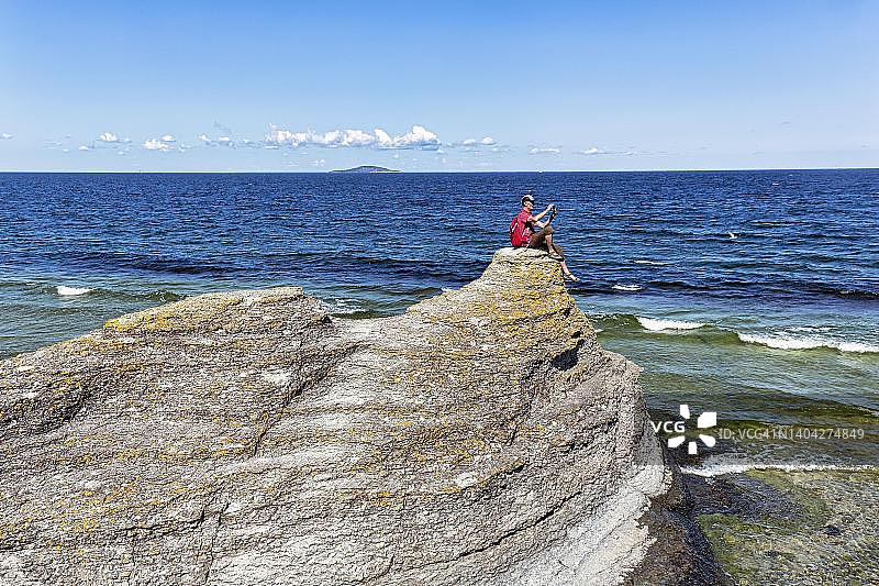 徒步旅行者坐在石灰岩柱上拍摄风景，位于瑞典卡尔马海峡岸边的劳卡尔，厄兰岛西海岸，比鲁姆图片素材