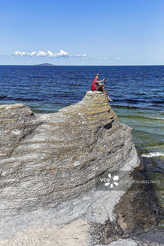 徒步旅行者坐在石灰岩柱上拍摄风景，位于瑞典卡尔马海峡岸边的劳卡尔，厄兰岛西海岸，比鲁姆图片素材