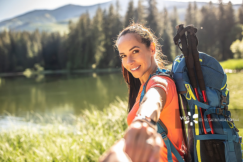 漂亮的女人徒步旅行者牵着男友的手，在森林湖边图片素材