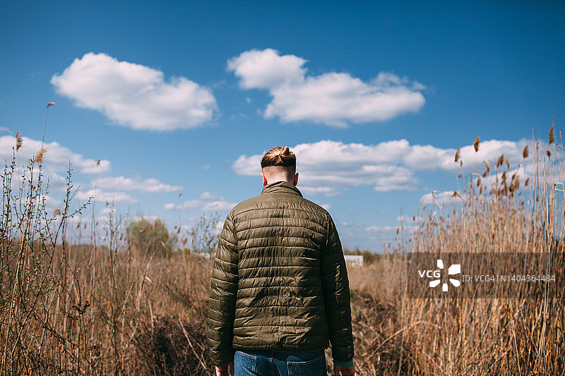 背对镜头站在干燥的田野和蓝天下的年轻男人图片素材