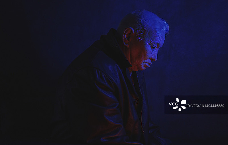 在黑色背景下，忧郁的年长男人被蓝色霓虹灯照亮图片素材