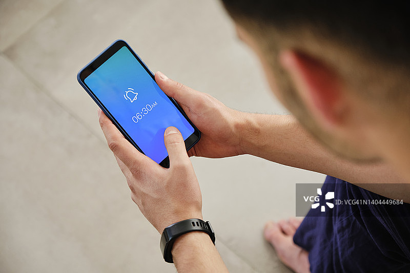 男人在家手持带有闹钟标志的手机图片素材
