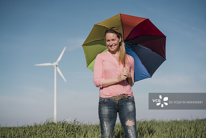 阳光明媚的日子里，笑容满面的女人在田野里撑着彩色雨伞图片素材
