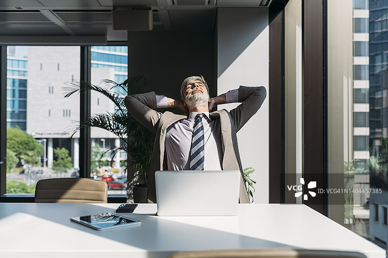 双手放在脑后，坐在办公室桌前的商人图片素材