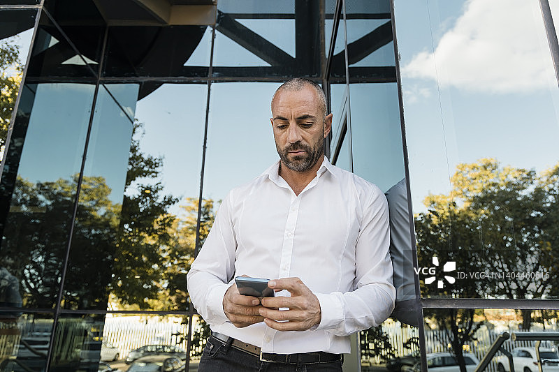 倚靠在玻璃墙上使用智能手机的男人图片素材