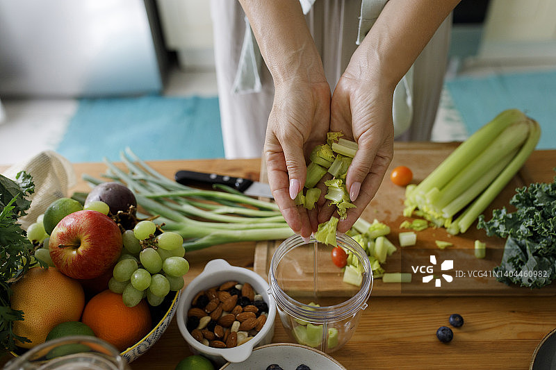 女人在家中将切碎的芹菜放入榨汁机图片素材