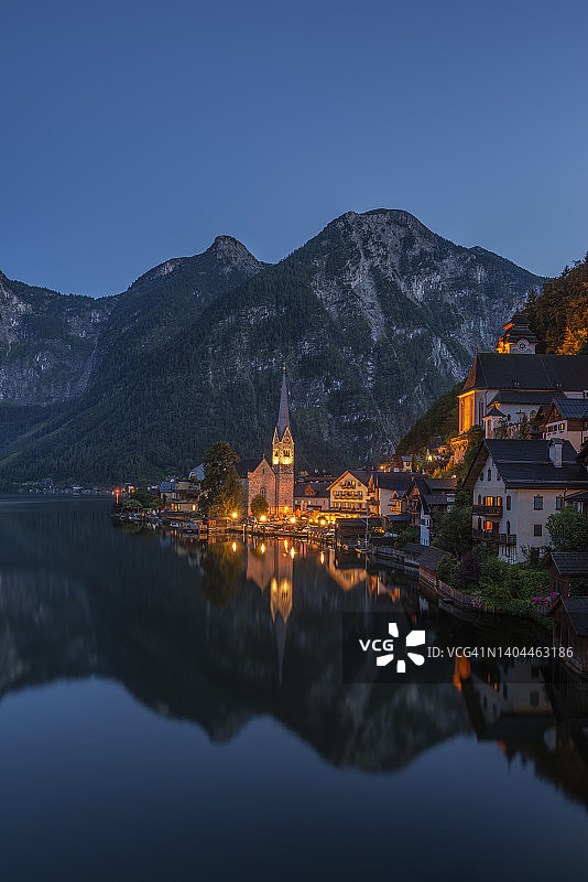 奥地利上奥地利州哈尔施塔特小镇黄昏湖岸景色，背景是灯火通明的教堂图片素材