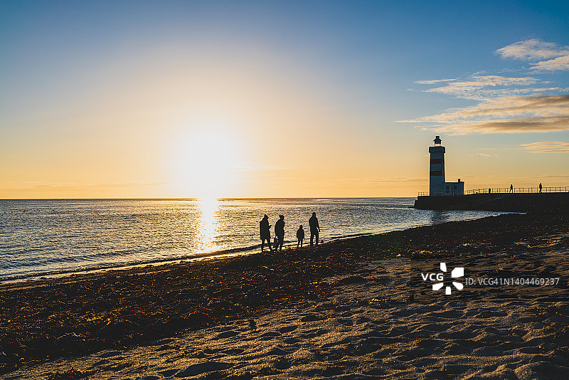 冰岛加尔泽灯塔的北冰洋午夜阳光景色，海滩上有一些剪影人像图片素材