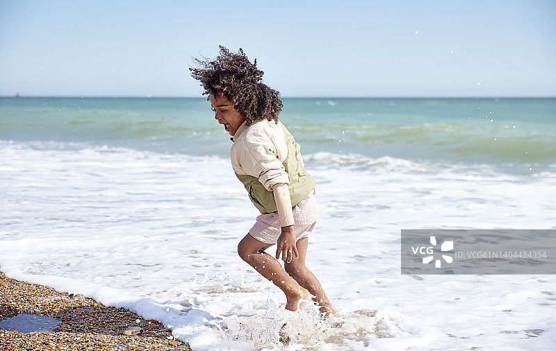 男孩在海滩上躲避涌入的白浪图片素材